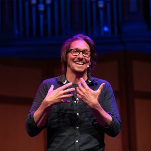 Image of a man on stage smiling and talking with his hands.