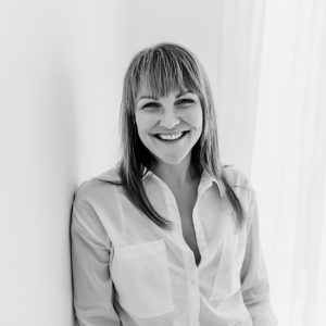 Black and white image of a woman with long hair and white shirt smiling at the camera.