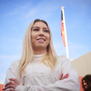 Image of a woman in a white jumper in front of a flag pole