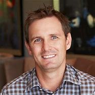Image of a man with short dark hair and a checked shirt smiling at the camera.