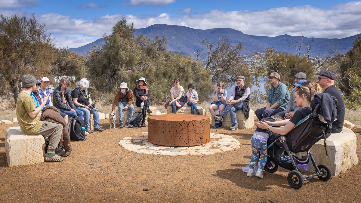 A group sit around a circular wall talking together. Mt Wellington is in the background.