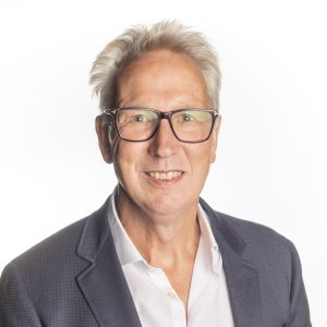 Image of a man with short spikey white hair, wearing glasses, a white shirt and grey jacket. The background is white.