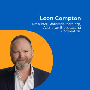 Image of a man with short hair and a beard wearing a white shirt and suit jacket, against an orange background.