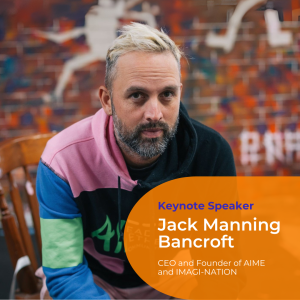 A portrait photo of Jack Manning Bancroft sitting in a wooden chair wearing a multicoloured hoodie, short spikey blonde hair with a beard and earring. He looks directly at the camera.