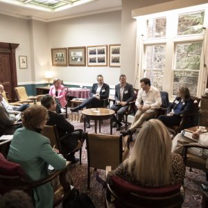 Photo taken in an old style clubroom with wooden chairs, tables and wood panelling. 5 panel speakers in front of participants in intimate setting.