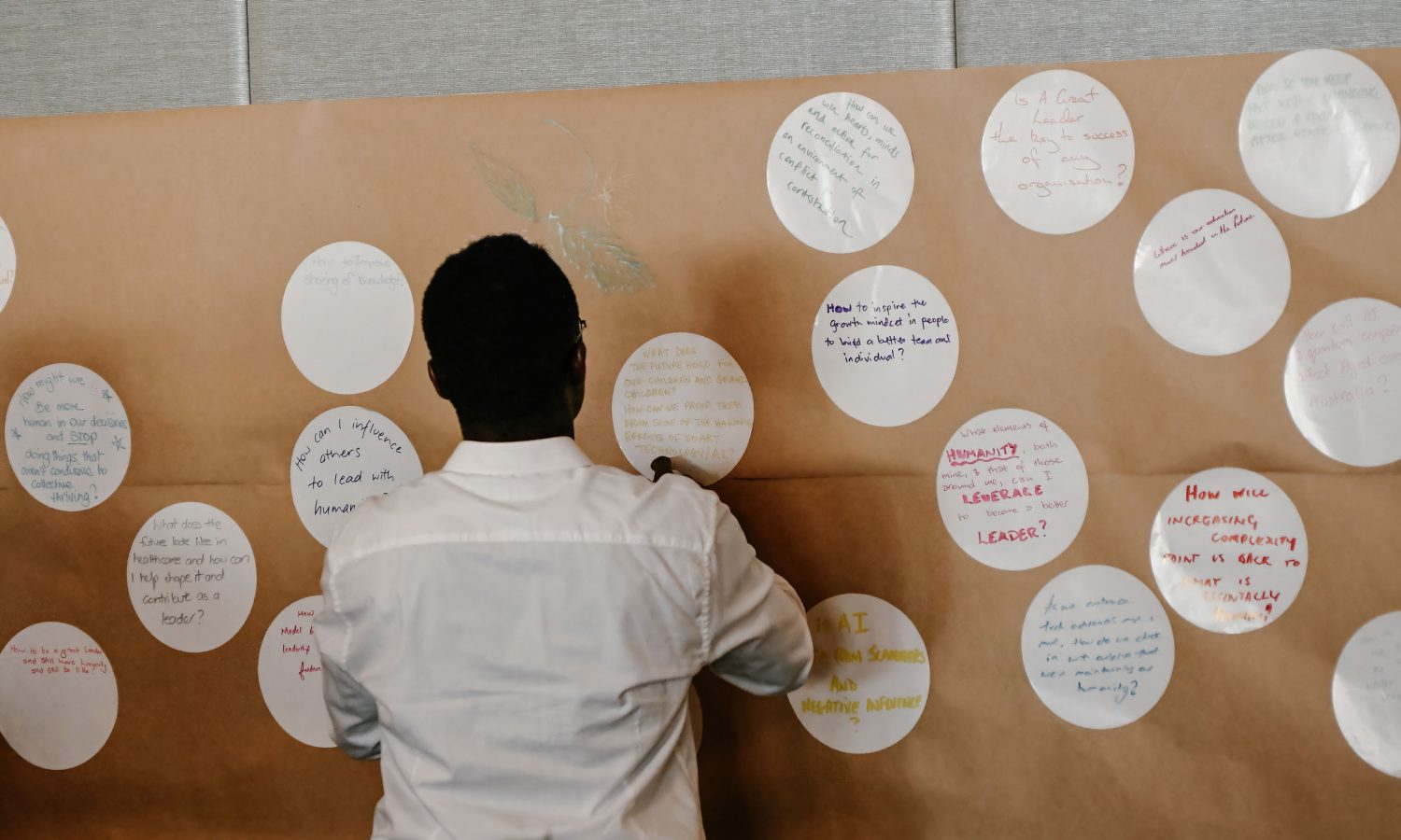 Photo of a man sticking a white circular sticker with writing on it onto a large roll of brown paper attached to a wall. There are many other white stickers on the brown paper.