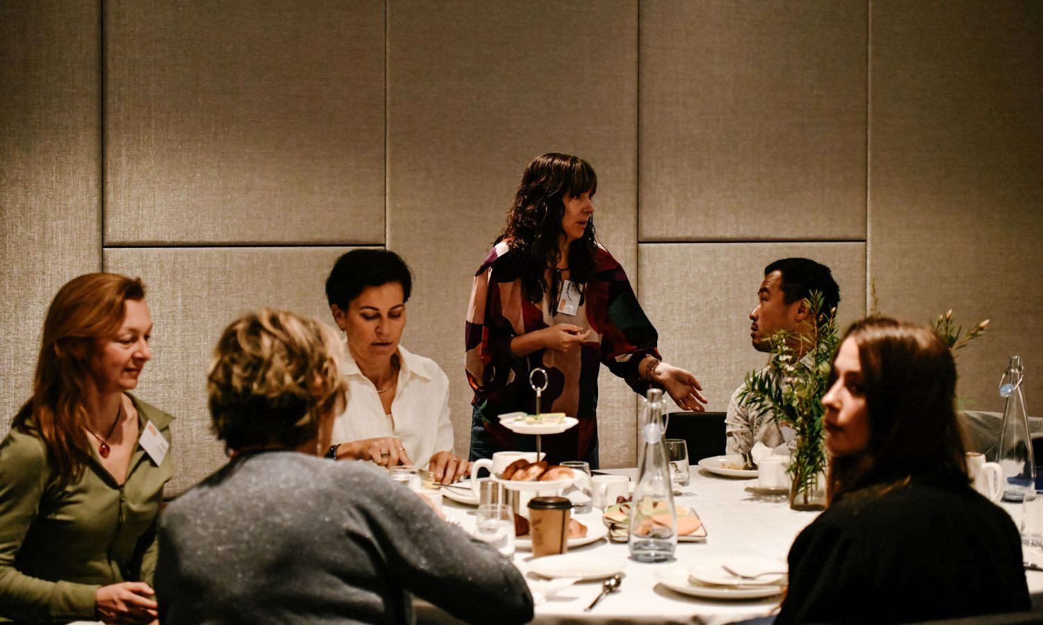 Image of 6 people around a round table two are talking together and the rest are eating.