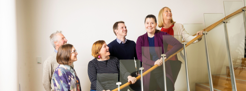 A landscape cropped photo of 6 graduates from 2024 Tasmanian Leaders Program on a wooden staircase. All smiling happily and looking up the stairs. Two men and four women are in the photo.