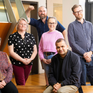 Photo of six participants from 2024 Tasmanian Leaders Program. Three women and three men standing together looking at the camera. Backdrop is a wooden and steel structure inside a building.