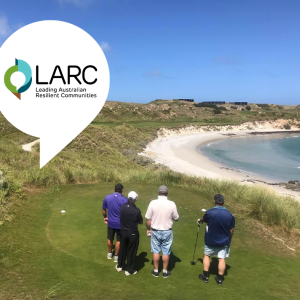 Photo of 4 golfers on a putting green overlooking a pristine beach. Blue sky, clear water and green grass.