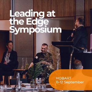 a photo of two panellists engaging with the facilitator behind a lectern on stage at the Symposium. smiling and listening to the facilitator.