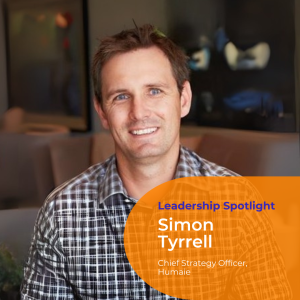 Portrait photo of Simon Tyrrell wearing a checked black and white shirt, with short dark hair and smiling directly at the camera.