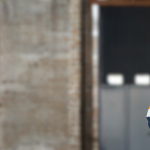 Image of a woman with short stylish hair, wearing a hi-vis workshirt. She stands with her arms crossed in front of an industrial site