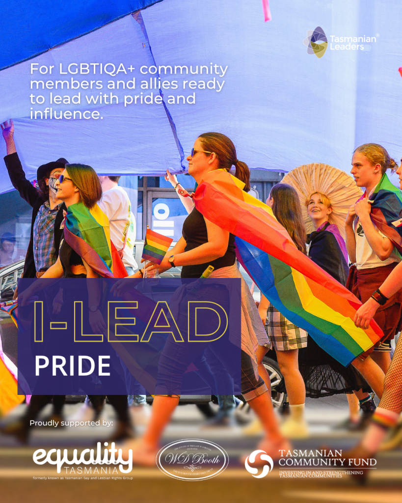 a group of people marching across the street. there is a large pride flag above their heads