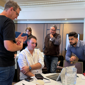 a group of people are standing and seated looking at a laptop and solving problems