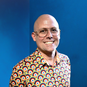 profile photo of Benny Callaghan. Benny is weraing a retro patterned shirt and glasses, with a bald head and a big smile