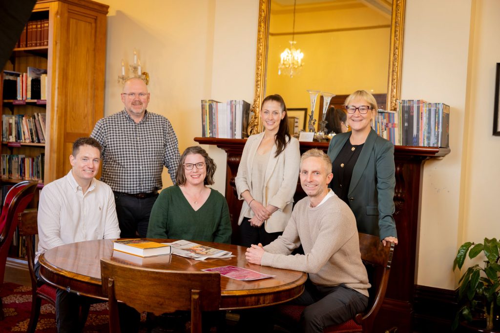 Photo of Nick Watson's Learning Set team - a group of people sitting and standing around a colonial style table in a heritage building.