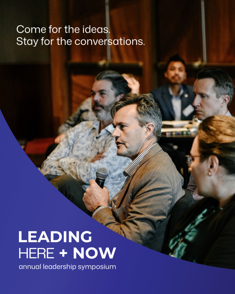 A participant speaks into a microphone during a Tasmanian Leaders event while others listen. Text reads “Come for the ideas. Stay for the conversations.” and “Leading Here + Now, annual leadership symposium.”