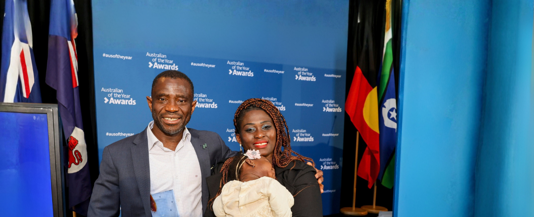 A man holding an Australian of the Year Award stands beside a smiling woman holding a baby at a Tasmanian Australian of the Year event.