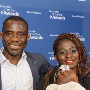 A man holding an Australian of the Year Award stands beside a smiling woman holding a baby at a Tasmanian Australian of the Year event.